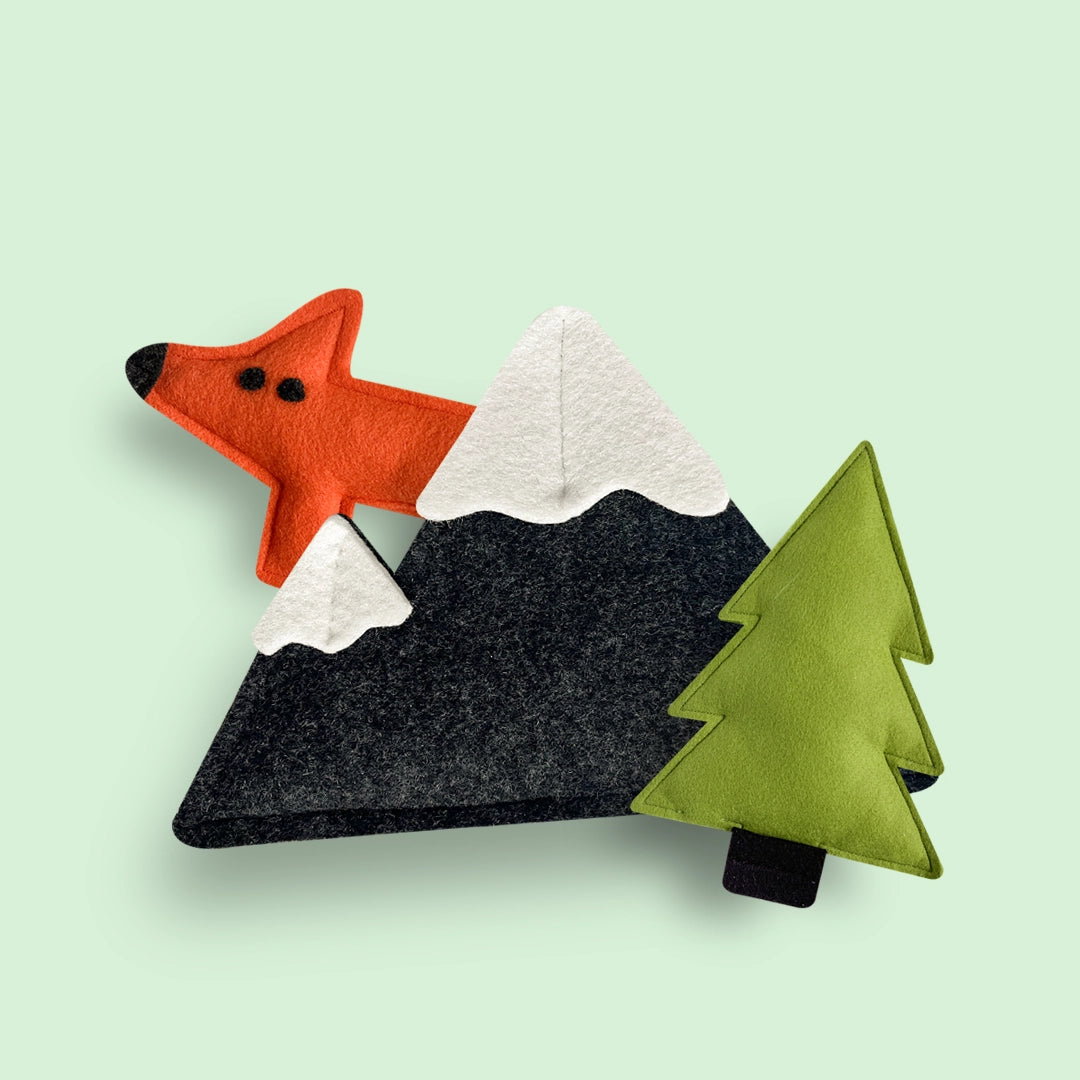Ručně vyráběné psí hračky. Hračky levitující na zeleném podkladu. Na obrázku je liška, hora a strom.